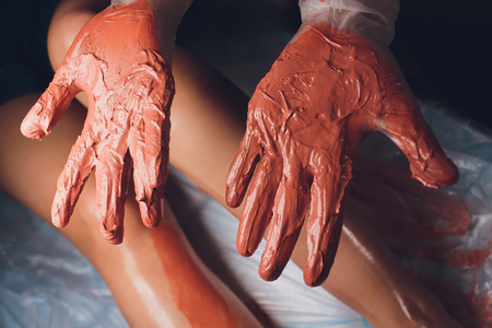 Young woman getting spa treatment in salon. Clay body mask applying by beautician. Mud therapy.の写真素材