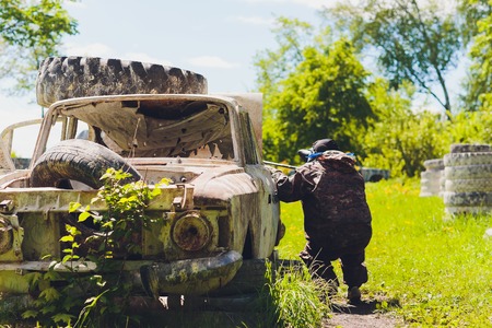 Paintball sport player in protective uniform and mask playing with gun outdoorsの写真素材