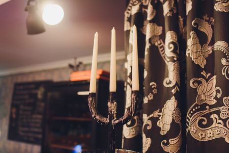 Triple vintage candlestick made of glass and black metal, two white stearin candles and one candle endの写真素材