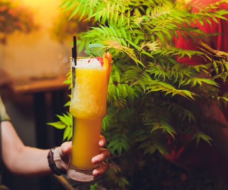 Woman hand holding orange cocktail decorated with mint in highball glass.