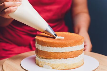 womens hands making biscuit cake with white cream using a cooking spatula.