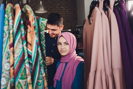 Smiling young muslim couple shopping and looking at carpets in a textile store.