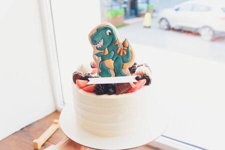 Children's holiday white cake decorated with mastic figurines of dinosaurs in the Jurassic period jungle. Concept ideas desserts for kidsの写真素材
