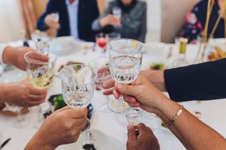 Close up shot of group of people clinking glasses with wine or champagne in front of bokeh background older people handsの写真素材