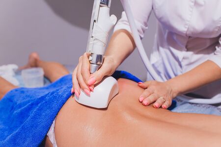 Cropped view of cosmetologist with roller doing buttocks starvac massage.