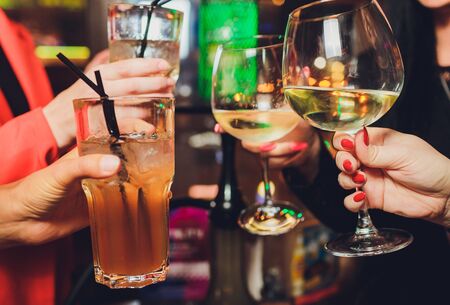 Close up shot of group of people clinking glasses with wine or champagne in front of bokeh...