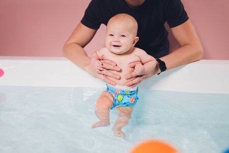 A father helps is infant boy during swimming lessons in the pool.