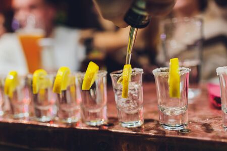 Bartender pouring strong alcoholic drink into small glasses on bar, shots.