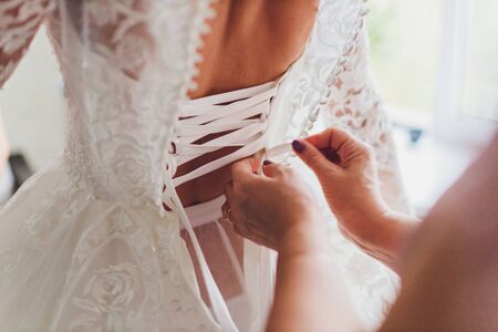 Buttoning the dress on bride. Details of beautiful lace wedding dressの写真素材