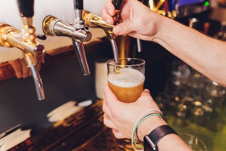Close up of a male bartender dispensing draught beer in a pub holding a large glass tankard under a spigot attachment on a stainless steel kegの写真素材