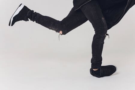 Close-up, Handsome young dancer dressed in black pants, a sweatshirt on a naked torso lifts one leg...