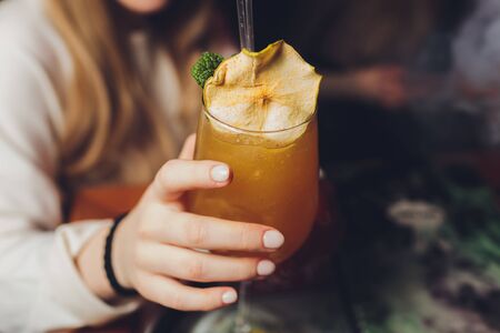 Womans hand holding old fashioned glass with cold cocktail against blurred night club background.