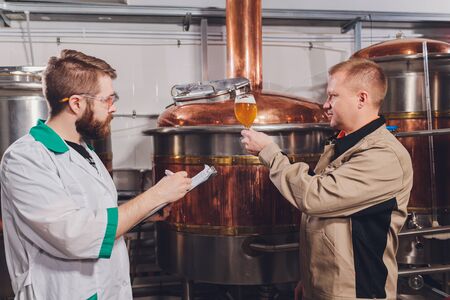 Mature man examining the quality of craft beer at brewery. Inspector working at alcohol manufacturing factory checking beer. Man in distillery checking quality control of draught beer.の写真素材