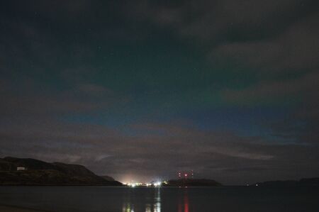 Aurora borealis over ocean. Northern lights in Teriberka, Russia. Starry sky with polar lights and clouds. Night winter landscape with aurora, sea with stones in blurred water, snowy mountains. Travelの写真素材