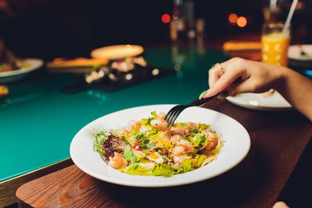 Restaurant or cafe table with plate of salads and wine. Two people talking on background. Toned picture.の写真素材