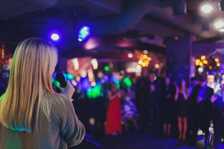 Backside view of adult female musician performing live on stage by singing a song in the microphone in front of an audience.の写真素材