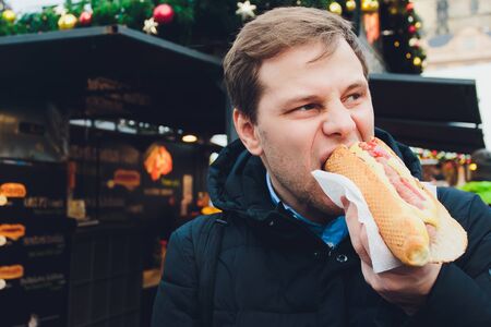 Closeup portrait of hungry man in glasses eating hot dog at outdoors background.の写真素材
