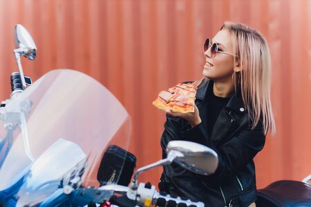 Girl eating a delicious pizza while sitting on a motorcycle.の写真素材
