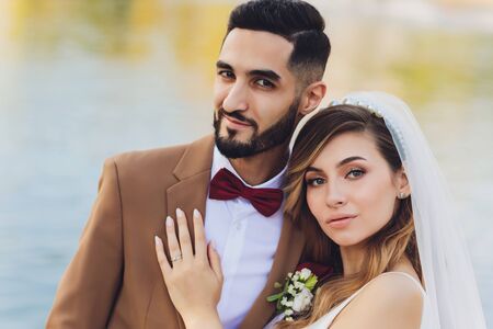 Stylish happy bride and groom posing at big love word in evening light at wedding reception outdoors. Gorgeous wedding couple of newlyweds having fun in evening park.の写真素材