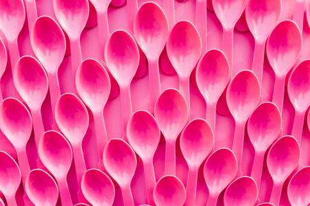 Plastic pink spoons in a row on pink background. Abstract conceptionの写真素材