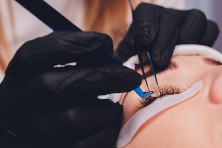 Eyelash Extension Procedure. Close up view of female eye with long eyelashes. Stylist holding pink...