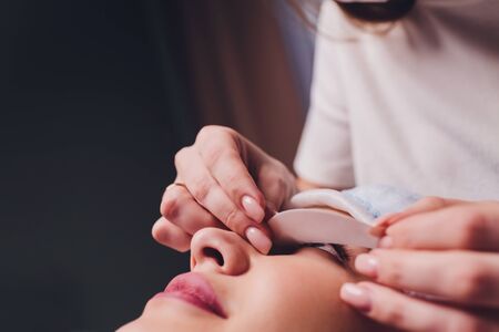 Eyelash Extension Procedure. Close up view of female eye with long eyelashes. Stylist holding pink...