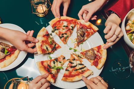 Flat lay with traditional Italian pizza with mussels, arugula and parmesan on dark blue stone table. Friends eating pizza. People's hands grabbing a slice of pizzaの写真素材
