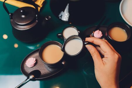 Woman pouring milk in mug of tea from kettleの写真素材