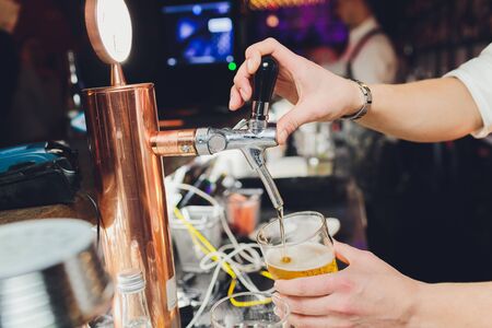 Close up of a male bartender dispensing draught beer in a pub holding a large glass tankard under a spigot attachment on a stainless steel keg.の写真素材