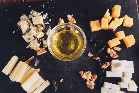 Assorted cheeses on round wooden board plate Camembert cheese, cheese grated bark of oak, hard cheese slices, walnuts, grapes, crackers, bread, thyme, dark black wood background, top viewの写真素材