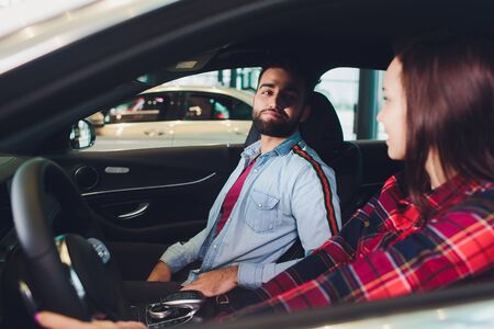 Visiting car dealership. Beautiful couple is talking and smiling while sitting in their new car. Woman driving her new car at the dealerの写真素材
