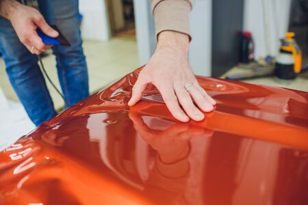 Car wrapping specialist putting vinyl foil or film on car wrapping protective film yacht, boat, ship, car, mobile home. orange film hand pullsの写真素材