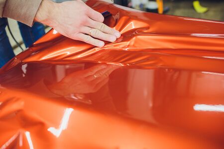 Car wrapping specialist putting vinyl foil or film on car wrapping protective film yacht, boat, ship, car, mobile home. orange film hand pullsの写真素材