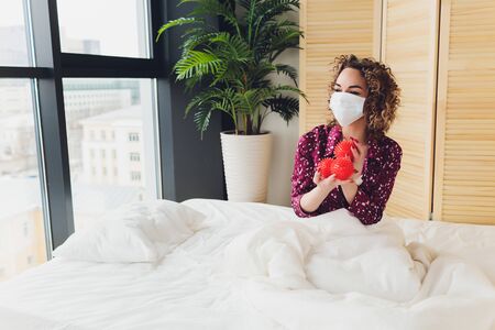 young beautiful sad and worried woman wearing medical face mask in quarantine and lock down at homeの写真素材