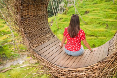 Young tourist enjoying her travel around Bali island , Indonesia. Making a stop on a beautiful hill overlooking a large lake. Photographs in a straw nest, natural environment. Lifestyle.の写真素材