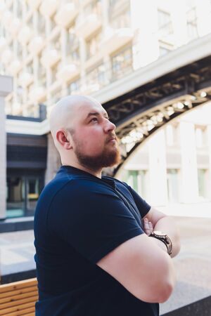 portrait of a bald handsome bearded man in a black t-shirt on the street, who looks away.の写真素材