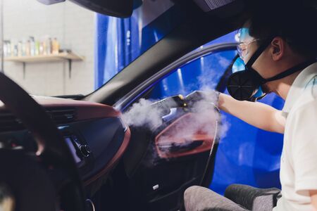 Disinfector in a protective suit and mask sprays disinfectants of car outdoors. Coronavirus Pandemic.の写真素材