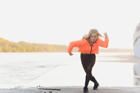 Healthy woman training on seaside promenade. Young attractive woman in sportswear does stretching...