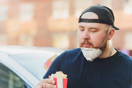 Young man tourist in medical mask eating street food on a walking street. Spicy fast food.の写真素材