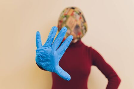 Girl in medical mask and gloves is looking at cameraand show her palm in stop gesture. Concept of fighting against virus due pandemic of coronavirus.の写真素材