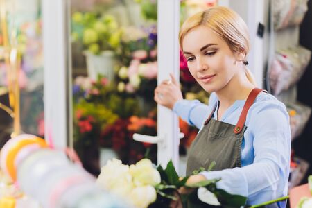 Female sales assistant working as florist and holding bouquet with customer in background. Horizontal shape, waist up.の写真素材