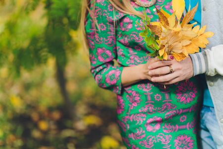Closeup on tummy of pregnant woman, wearing long green dress, holding in hands bouquet of daisy flowers outdoors, new life concept.の写真素材