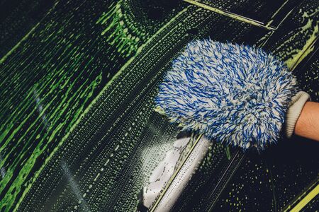 Car wash by hand. Soap suds, bubbles and mitt. Man washing a car by hand.
