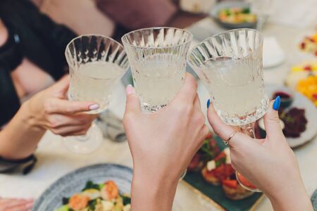 Close up shot of group of people clinking glasses with wine or champagne in front of bokeh...