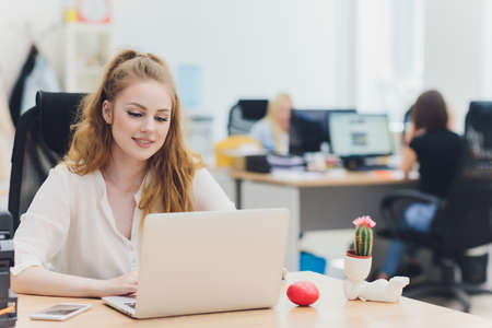 Portrait of a serious businesswoman using laptop in office. Beautiful hipster woman taking notes at...