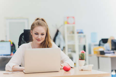 Portrait of a serious businesswoman using laptop in office. Beautiful hipster woman taking notes at...