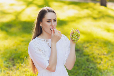 Smiling woman having a relaxing lunch break outdoors, she is sitting on the grass and eating.の写真素材