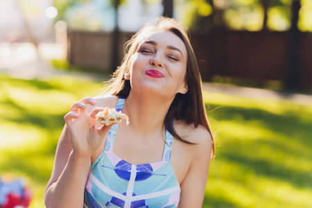 Smiling woman having a relaxing lunch break outdoors, she is sitting on the grass and eating.