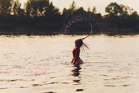Beautiful young woman in red swimsuit posing near river. Summer lifestyle.の写真素材