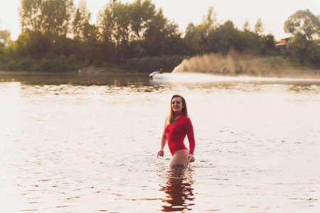 Beautiful young woman in red swimsuit posing near river. Summer lifestyle.の写真素材